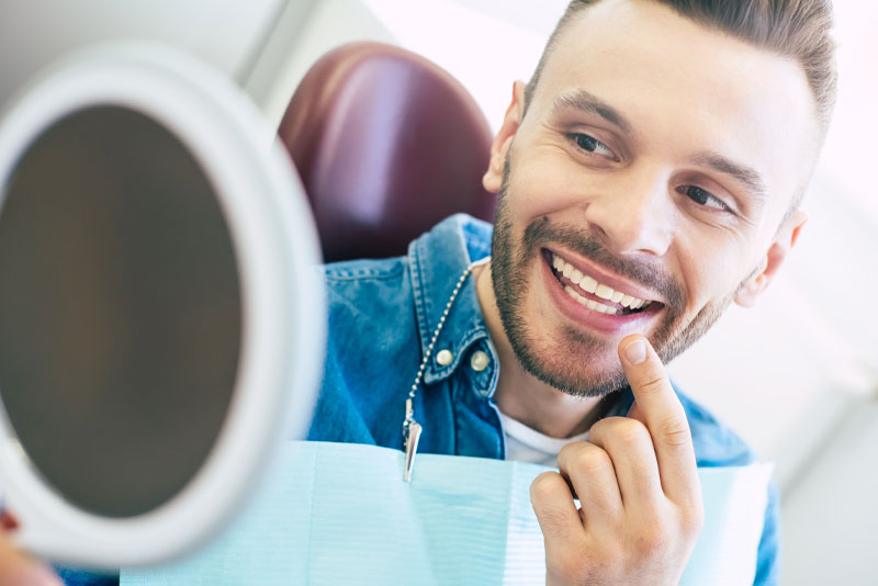 image of a dental patient smiling into a mirror and pointing at his teeth because he just got dental veneers placed