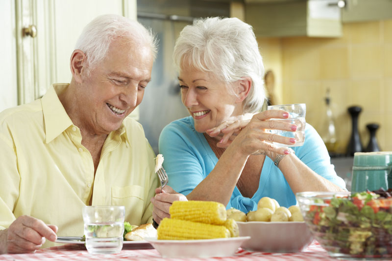 an elderly couple smiling at each other over dinner because they have been treated with cost-effective dental implants.